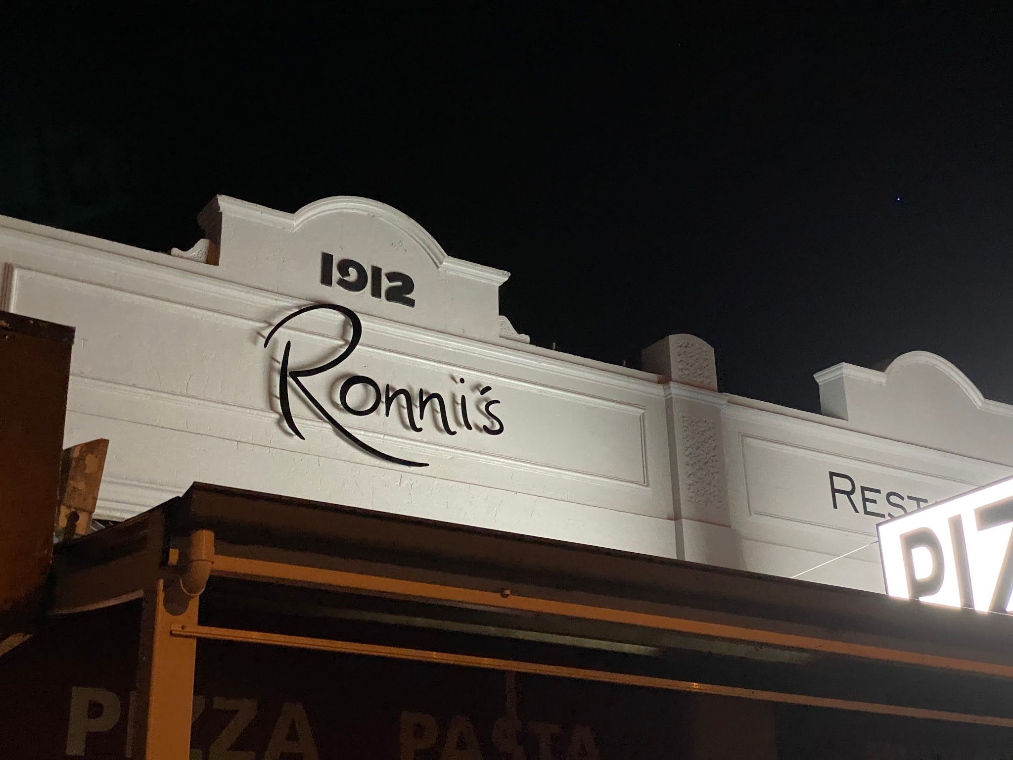 Ronni's Restaurant heritage facade at night showing 1912 parapet and Pizza Pasta signage