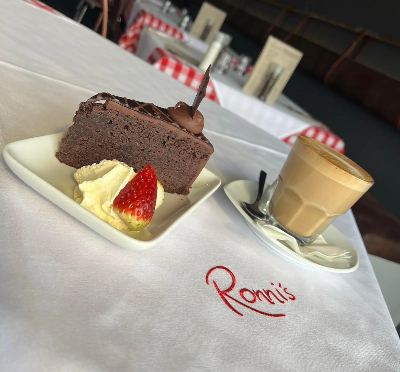 Chocolate cake slice with strawberry and latte on Ronni's embroidered white tablecloth