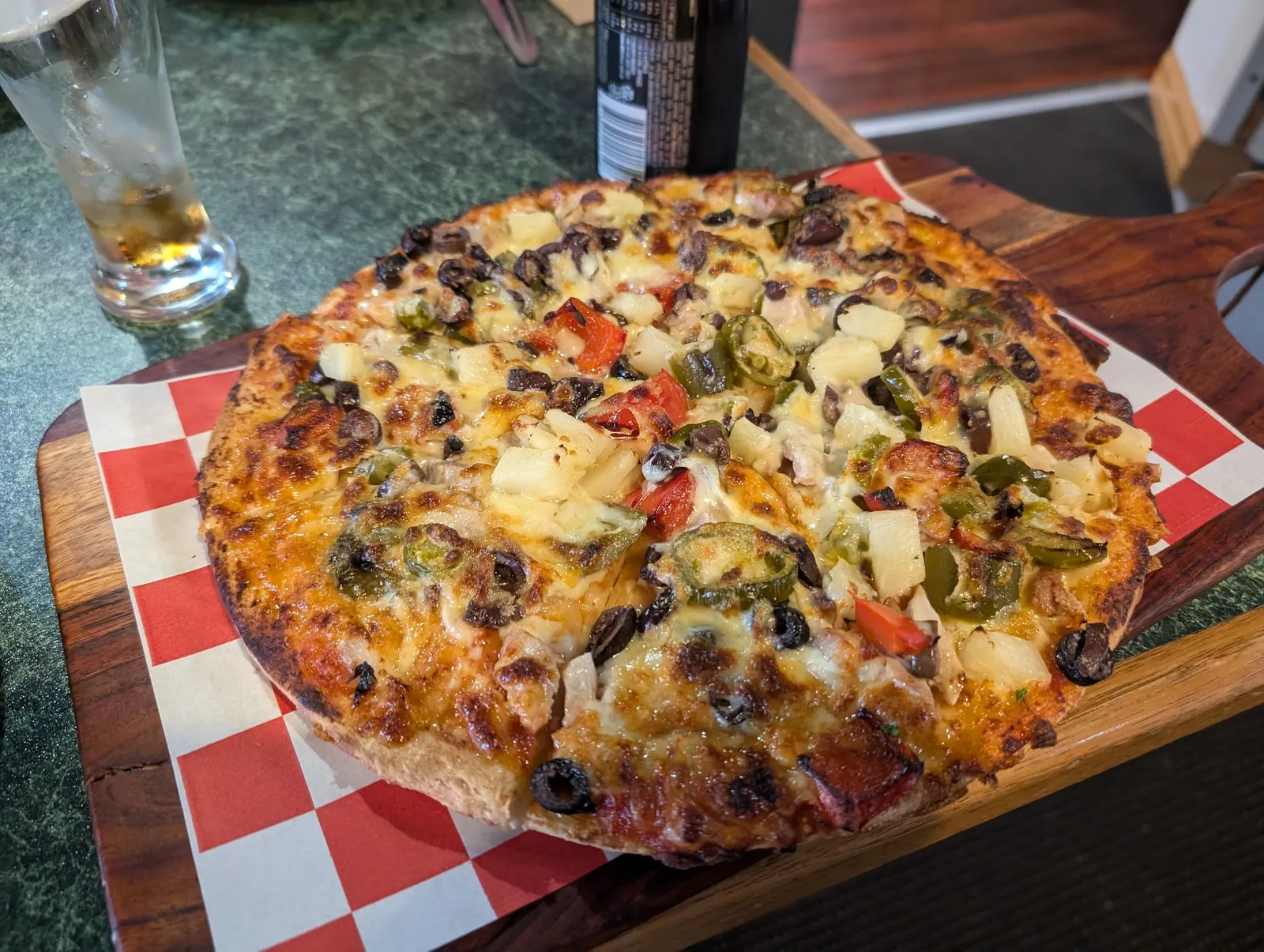 Fully-loaded pizza with cheese, olives, capsicum and pineapple on wooden board