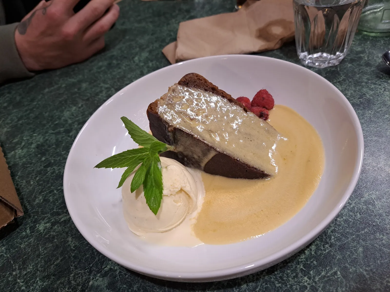 Chocolate mud cake with brulee top and raspberries in cream anglaise on green marble