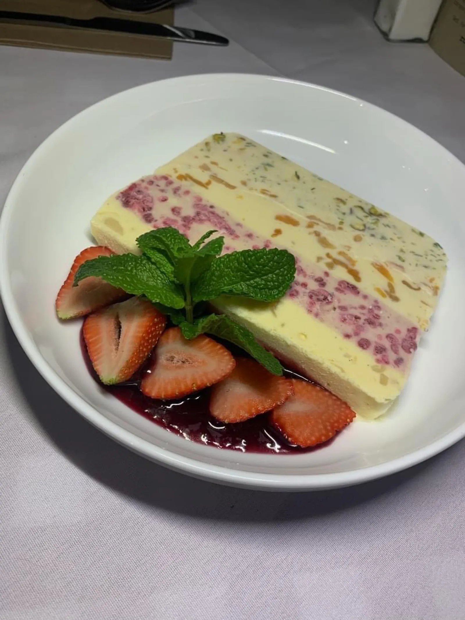 Semifreddo ice cream terrine with strawberries and berry coulis in a white bowl