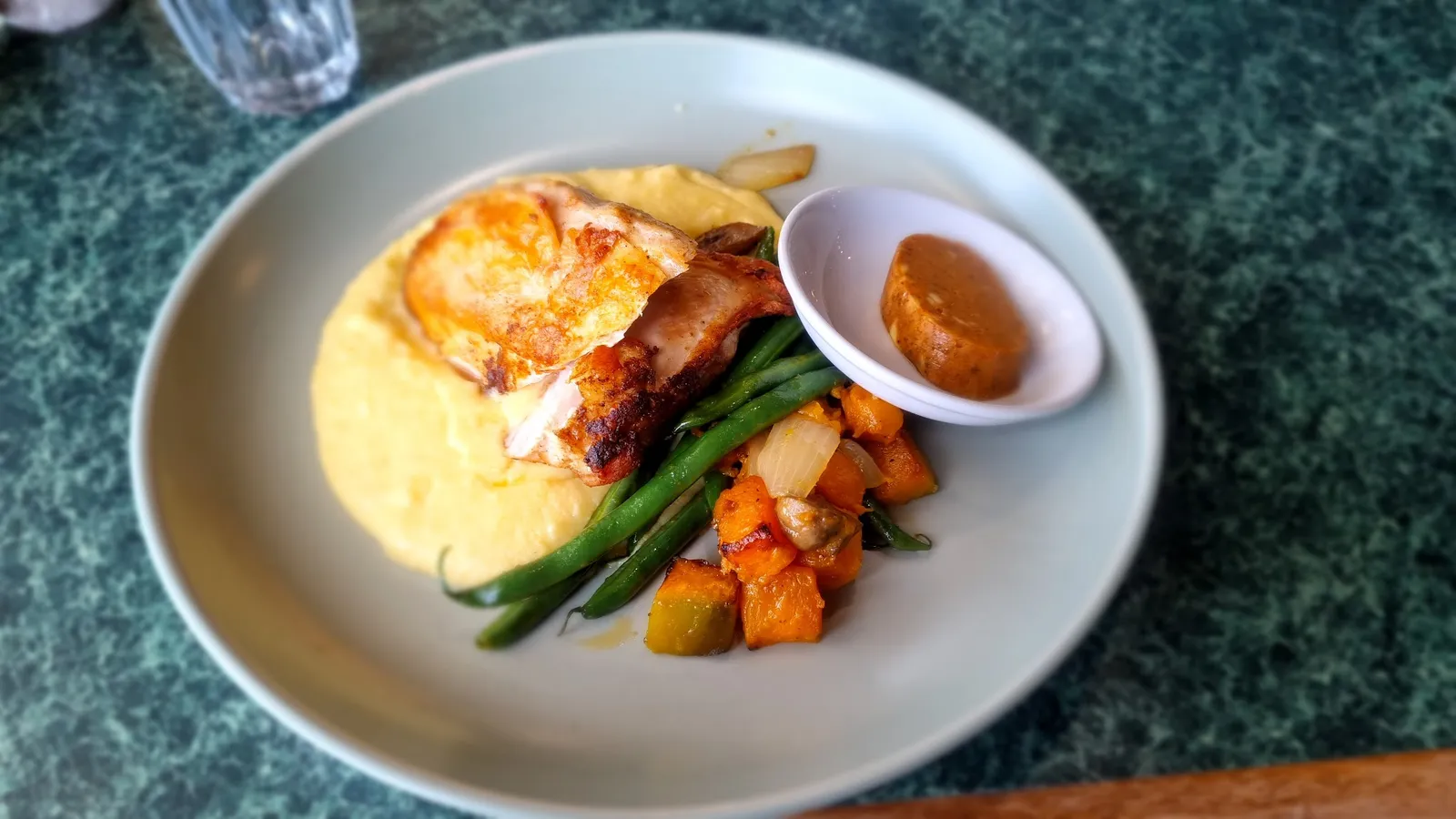 Roasted chicken on creamy polenta with pumpkin, beans and sauce on green marble