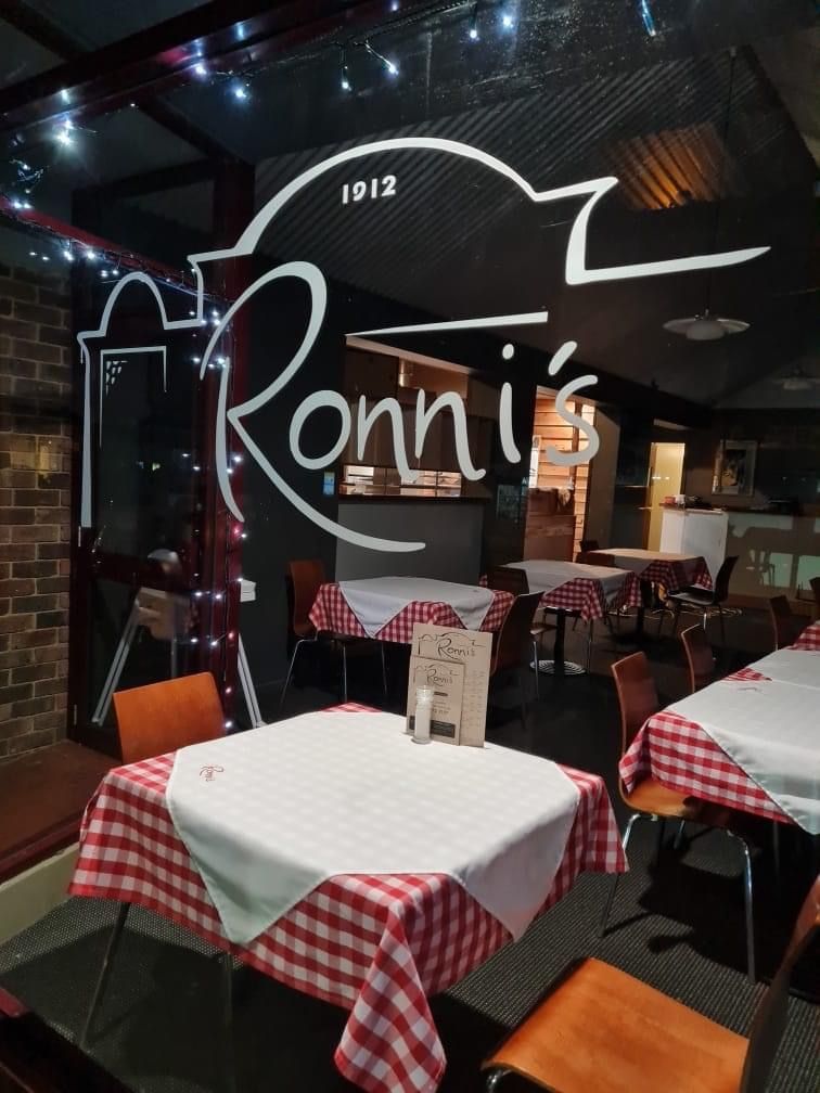 Ronni's dining room at night through glass with 1912 logo, gingham tables and fairy lights