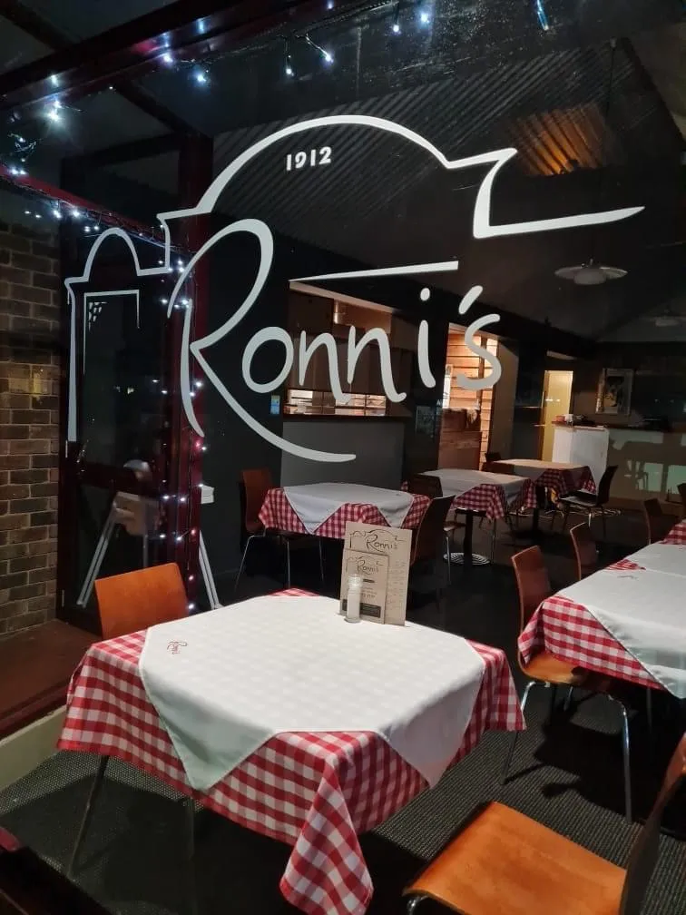Ronni's dining room at night through glass with 1912 logo, gingham tables and fairy lights
