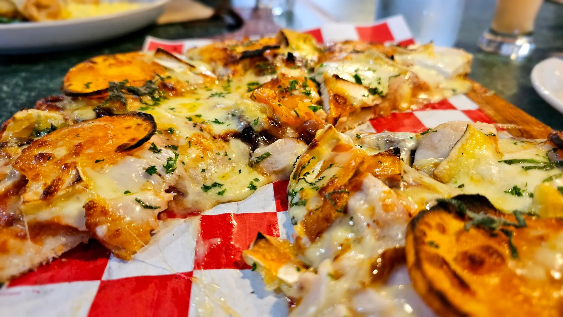 Thin-crust pizza with pumpkin, mushroom, chicken and blue cheese from table-level angle