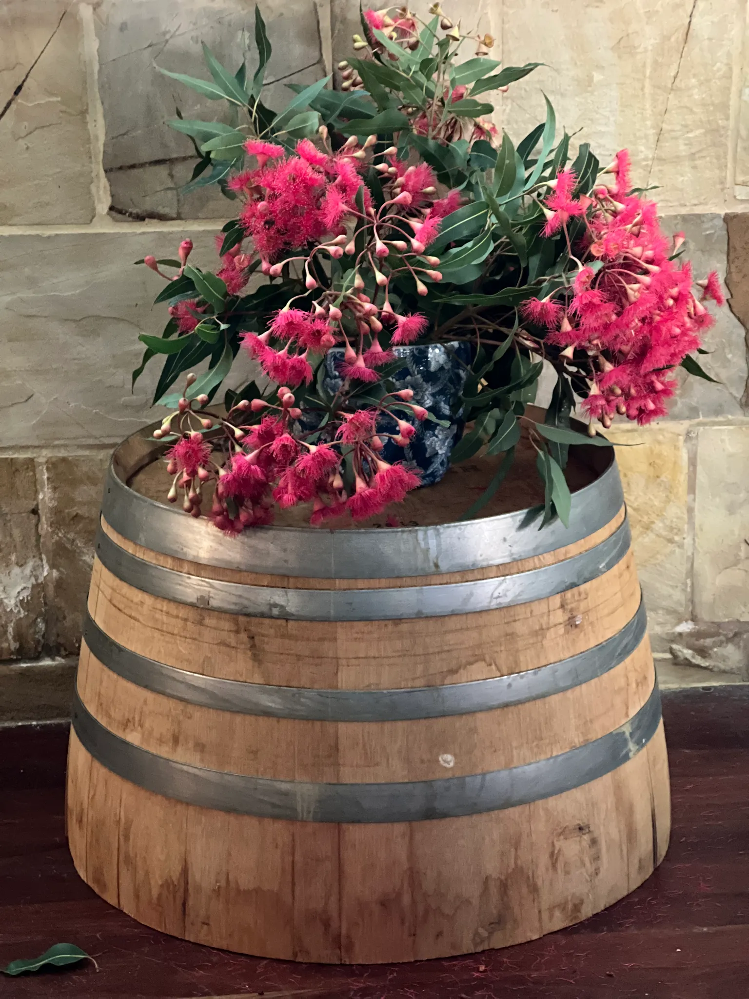 Wine barrel with pink native flowering gum branches against sandstone wall inside Ronni's