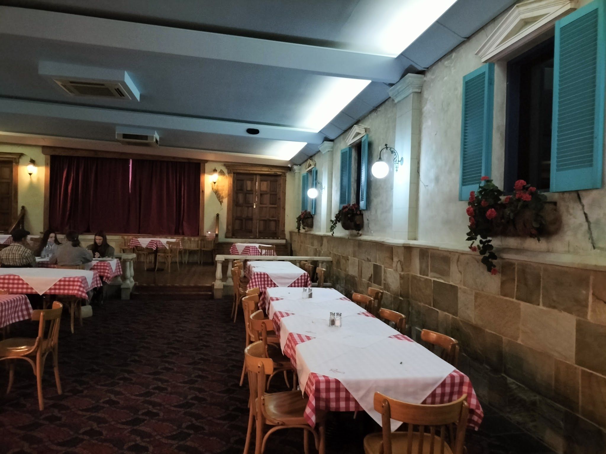Ronni's dining room with stone walls, teal shuttered windows, gingham tables and seated diners