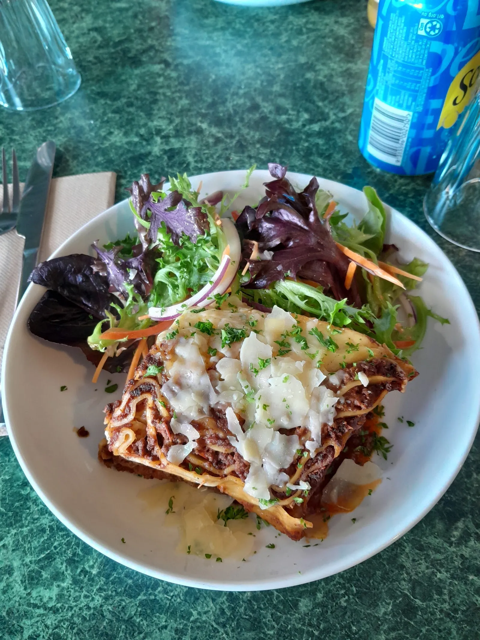 Creamy lasagne with parmesan and herbs alongside fresh salad on green marble