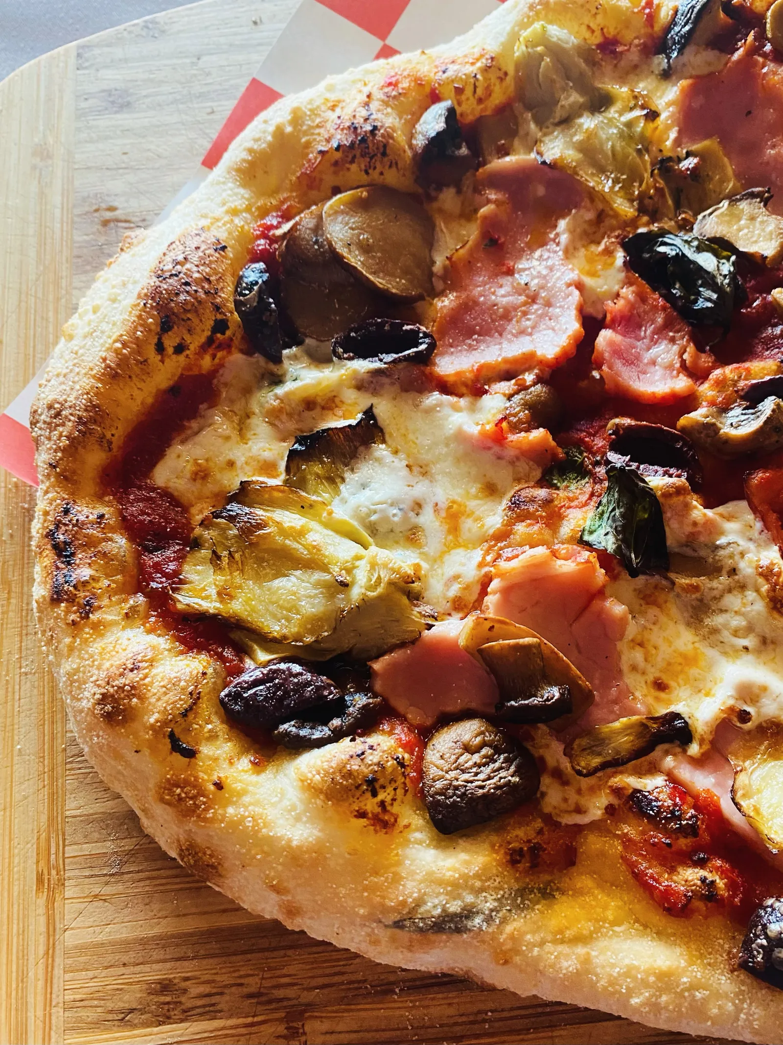 Wood-fired pizza with ham, artichoke, mushrooms and olives on a wooden board