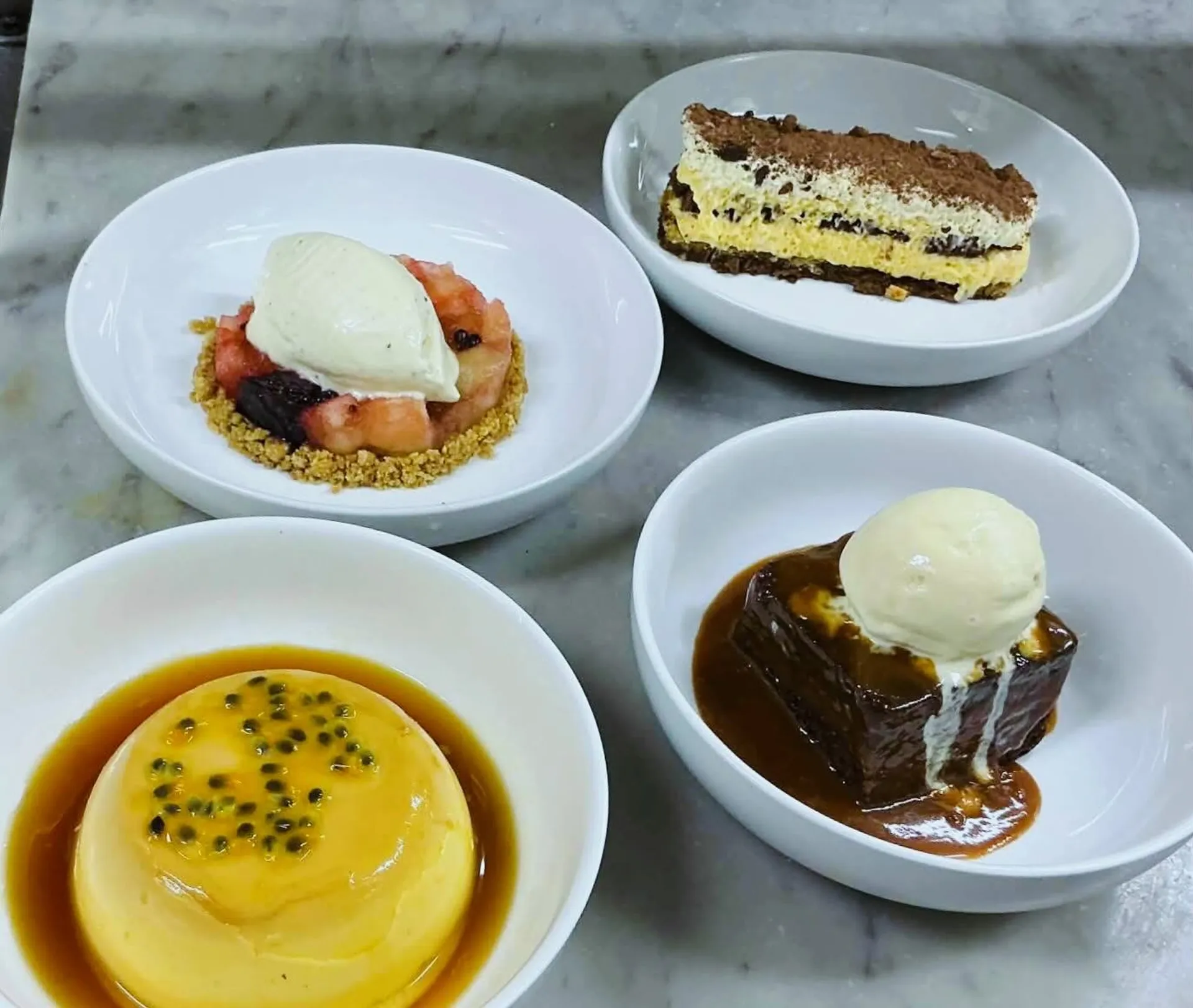 Four Italian desserts on marble: tiramisu, creme caramel, sticky date and berry cream