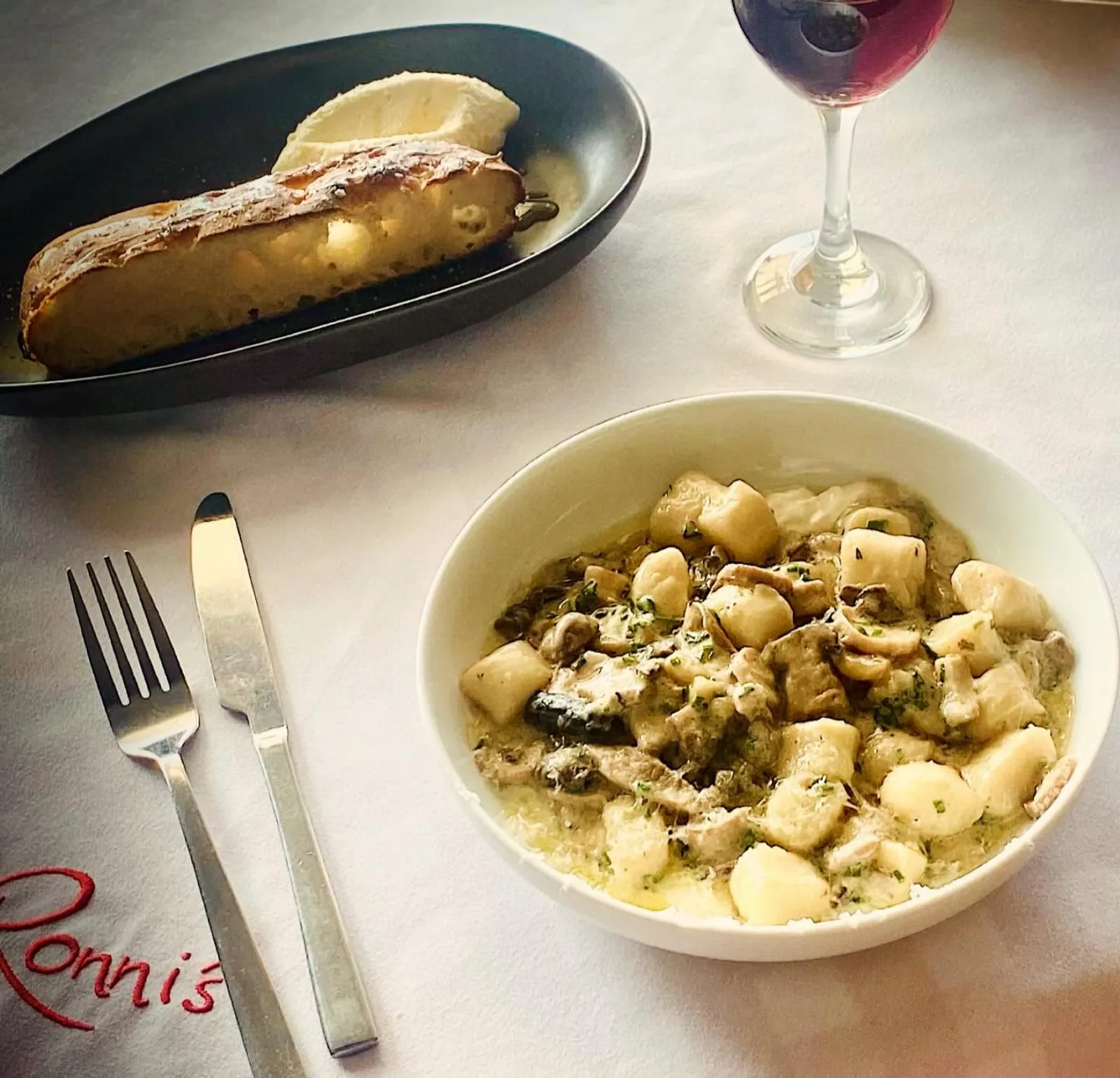 Gnocchi in creamy mushroom sauce with garlic bread and red wine in background